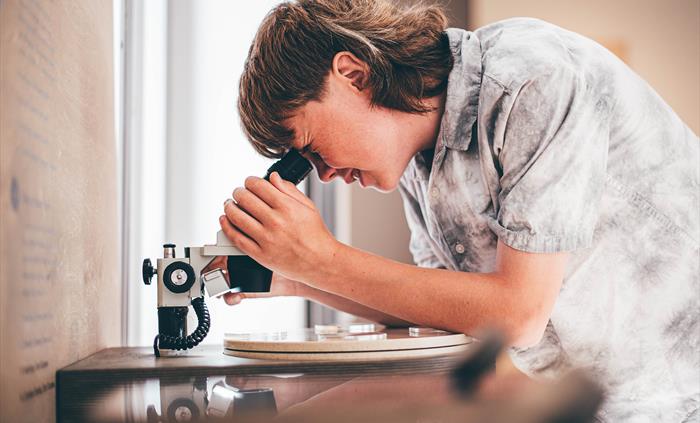 A teenage boy looking into a microscope.